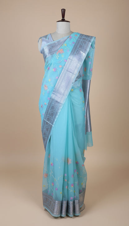 Light blue saree with a border on a mannequin against a patterned wall.