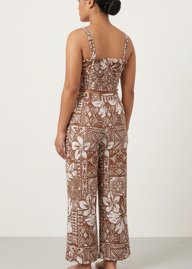 A woman shown from the back wearing a sleeveless wide-leg jumpsuit with a brown and beige floral and geometric pattern, standing against a plain white studio background.