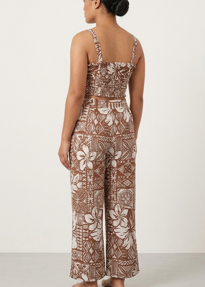 A woman shown from the back wearing a sleeveless wide-leg jumpsuit with a brown and beige floral and geometric pattern, standing against a plain white studio background.
