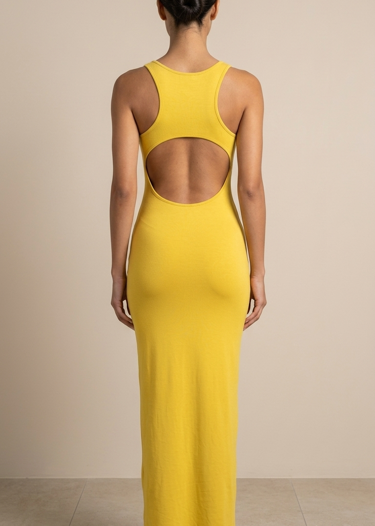 A woman viewed from the back wearing a bright yellow sleeveless maxi dress with a large open back cutout, standing against a plain beige studio wall.